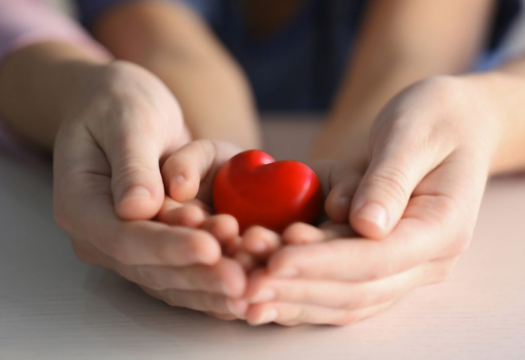 Child and adult person holding red heart, closeup. Adoption concept